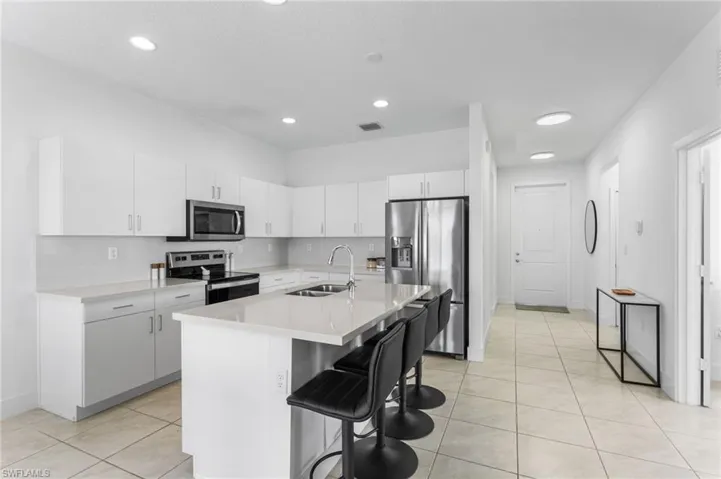 Kitchen featuring white cabinets, stainless steel appliances, a breakfast bar area, an island with sink, and light tile patterned floors