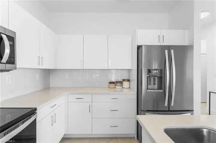 Kitchen featuring stainless steel appliances, white cabinetry, light tile patterned floors, and tasteful backsplash