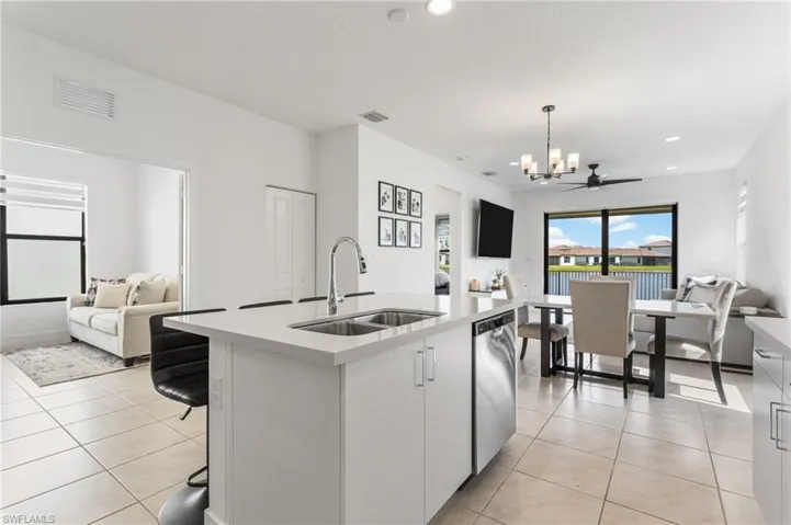 Kitchen featuring open floor plan, an island with sink, light stone counters, suspended lighting, and white cabinets