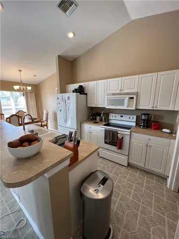Kitchen with white appliances, white cabinets, a center island with sink, light countertops, and lofted ceiling