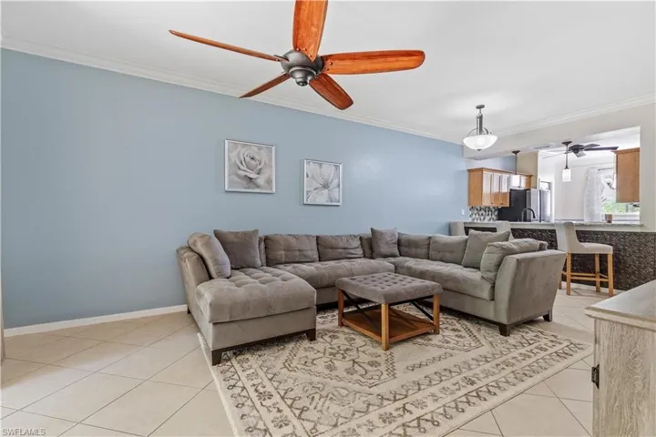 Living room with crown molding, light tile patterned floors, and ceiling fan