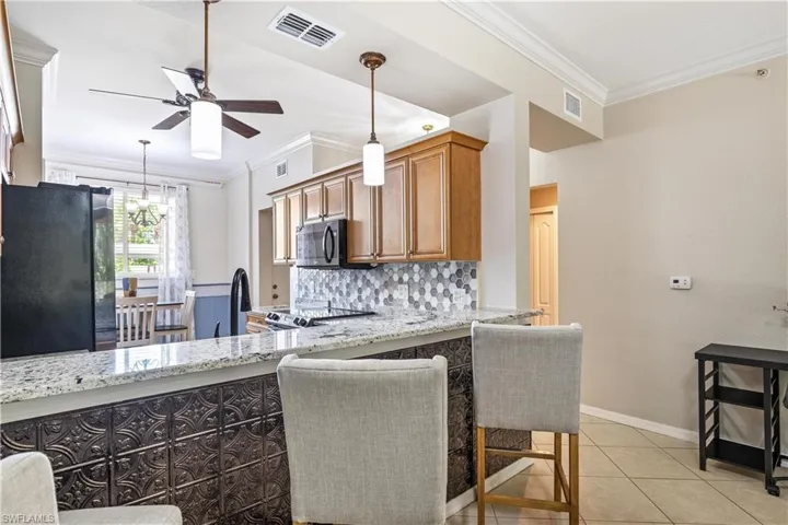 Kitchen featuring ceiling fan, hanging light fixtures, decorative backsplash, black fridge, and light tile patterned floors