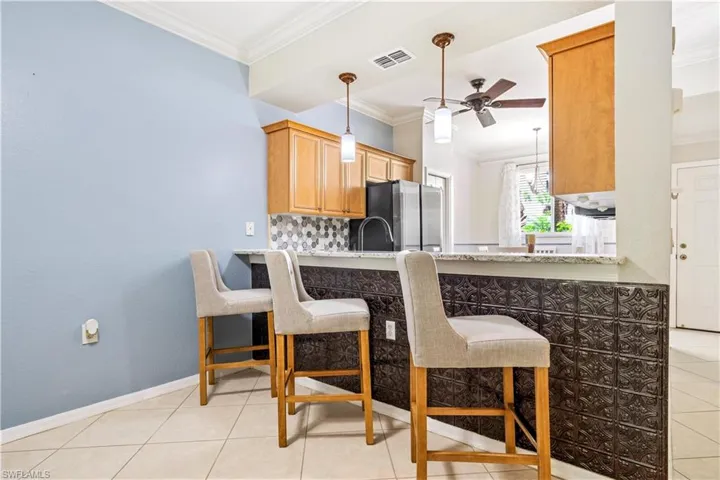 Kitchen with light tile patterned flooring, a breakfast bar area, ceiling fan, stainless steel fridge, and decorative light fixtures