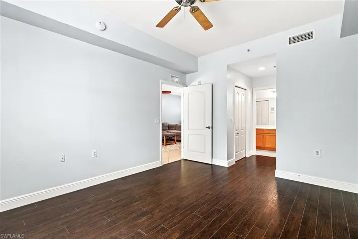 Unfurnished bedroom with a closet, ensuite bath, ceiling fan, and dark wood-type flooring