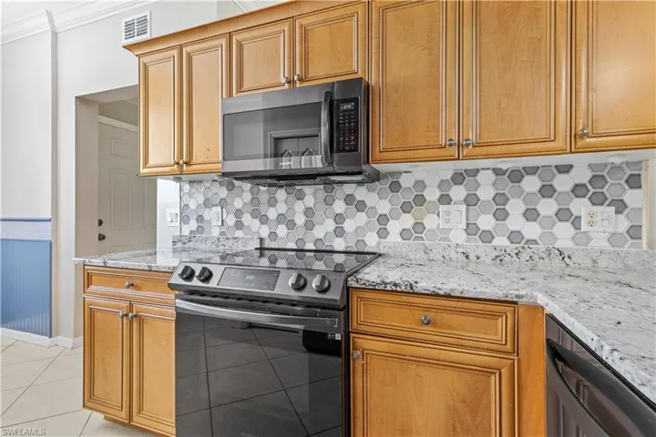 Kitchen with crown molding, tasteful backsplash, light tile patterned floors, light stone counters, and black range with electric cooktop