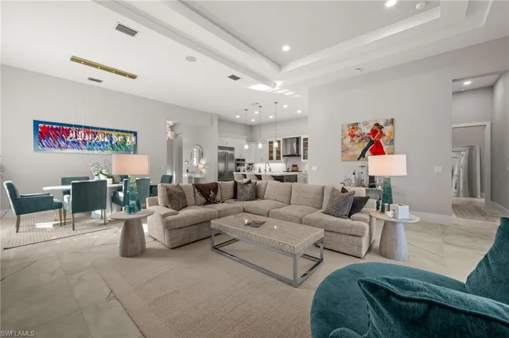 Open-concept living space with large format tile flooring, tray ceiling, recessed lighting, and a modern dining area chandelier