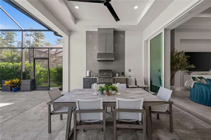 Covered outdoor living space featuring an integrated kitchen with a stainless steel grill and range hood, screened enclosure, ceiling fan, and recessed lighting