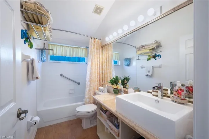 Full bath with visible vents, toilet, shower / bath combo with shower curtain, vaulted ceiling, and wood finished floors