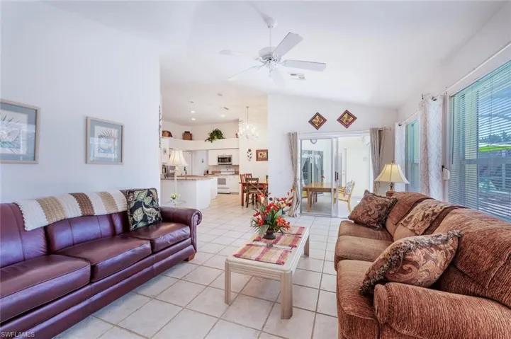 Living area featuring light tile patterned floors, visible vents, ceiling fan with notable chandelier, and vaulted ceiling
