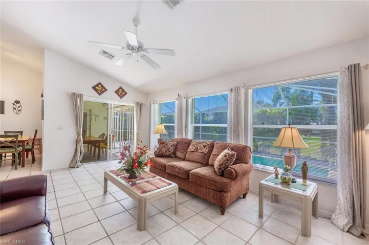 Living area with vaulted ceiling, light tile patterned floors, a ceiling fan, and visible vents