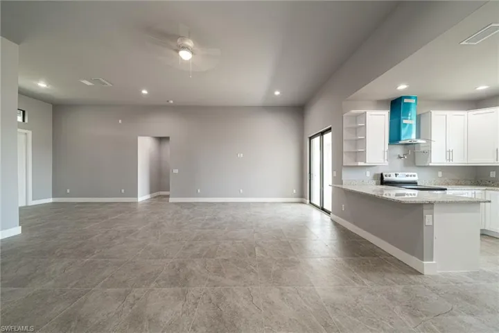 Kitchen with a peninsula, a ceiling fan, light stone countertops, open shelves, and white cabinets