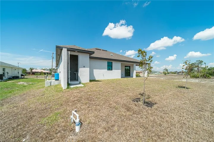 Back of property featuring a yard, stucco siding, and roof with shingles