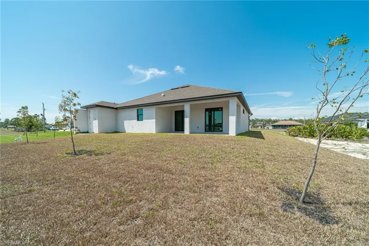 Rear view of house featuring stucco siding, a lawn, and a patio