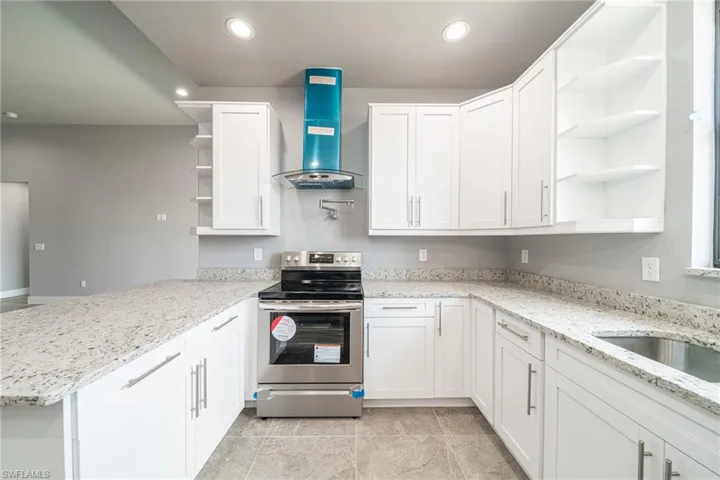 Kitchen featuring open shelves, electric range, light stone counters, ventilation hood, and white cabinetry