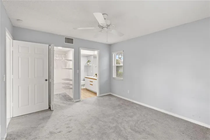 Unfurnished bedroom with light colored carpet, connected bathroom, ceiling fan, and a textured ceiling