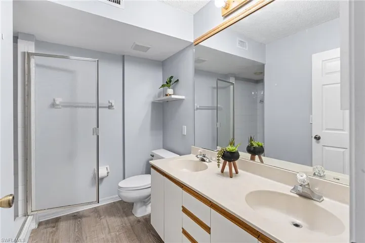 Bathroom with light wood-type flooring, double vanity, a shower stall, and a textured ceiling