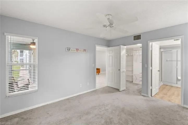 Unfurnished bedroom with carpet, a ceiling fan, a spacious closet, and ensuite bath