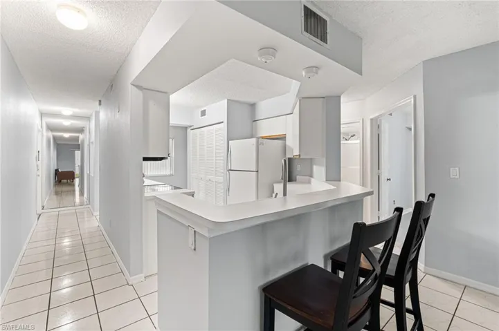 Kitchen with light tile patterned flooring, a textured ceiling, a kitchen breakfast bar, light countertops, and freestanding refrigerator
