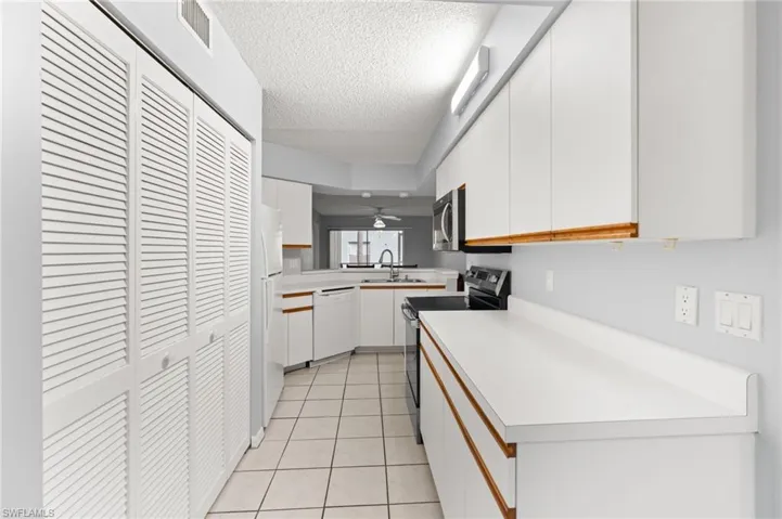 Kitchen with white cabinetry, light countertops, white appliances, light tile patterned flooring, and a textured ceiling