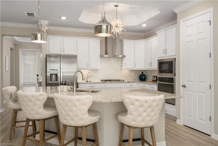 Kitchen with crown molding, wall chimney range hood, a tray ceiling, light hardwood / wood-style floors, and appliances with stainless steel finishes