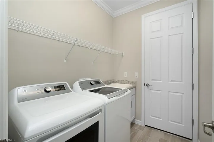 Clothes washing area with crown molding, light hardwood / wood-style flooring, washing machine and dryer, cabinets, and sink