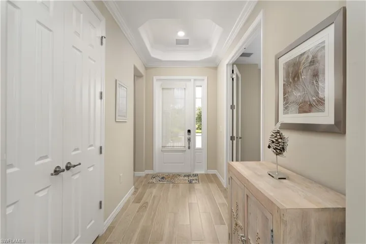 Entrance foyer with ornamental molding, light hardwood / wood-style flooring, and a raised ceiling