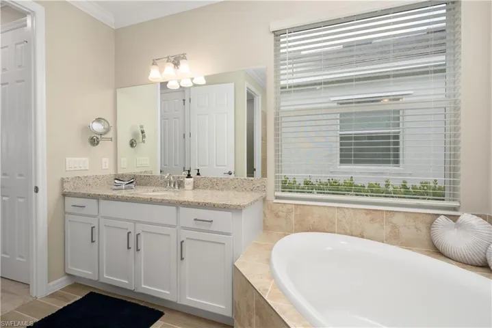 Bathroom featuring vanity, crown molding, and tiled bath