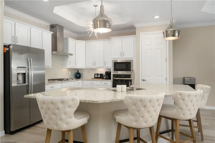 Kitchen featuring stainless steel appliances, wall chimney range hood, light hardwood / wood-style floors, white cabinetry, and a tray ceiling