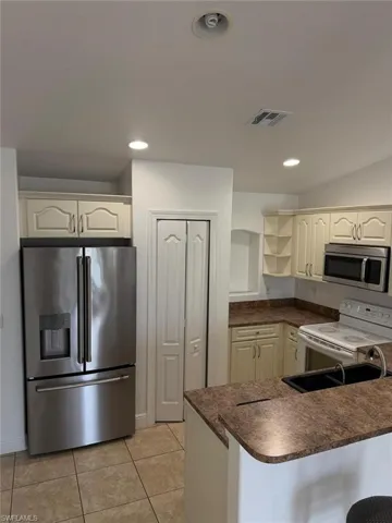 Kitchen featuring neutral-toned cabinetry, granite-style countertops, stainless steel microwave, and a breakfast bar