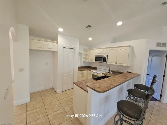 Kitchen featuring neutral-toned cabinetry, granite-style countertops, stainless steel microwave, and a breakfast bar...refrigerator in previous pictures