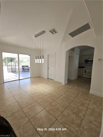 Open-concept interior featuring large format tile flooring, a modern linear pendant light fixture, and an arched doorway