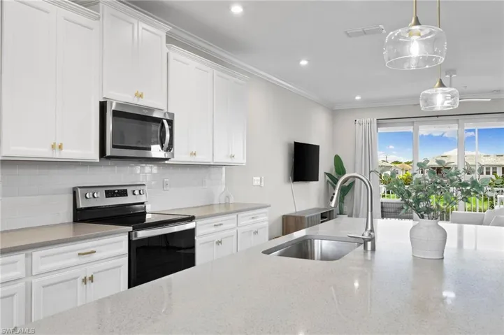 Kitchen with appliances with stainless steel finishes, backsplash, light stone counters, white cabinetry, and crown molding