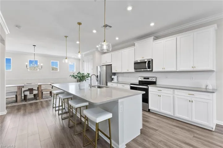 Kitchen with a kitchen breakfast bar, appliances with stainless steel finishes, a kitchen island with sink, pendant lighting, and white cabinetry