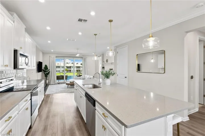 Kitchen with a center island with sink, white cabinets, stainless steel appliances, light stone counters, and crown molding