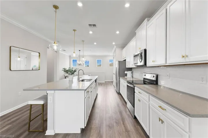 Kitchen featuring stainless steel appliances, a kitchen bar, an island with sink, white cabinets, and recessed lighting