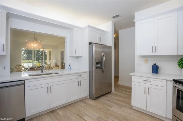 Kitchen featuring stainless steel appliances, a chandelier, white cabinets, light stone countertops, and light wood-style flooring