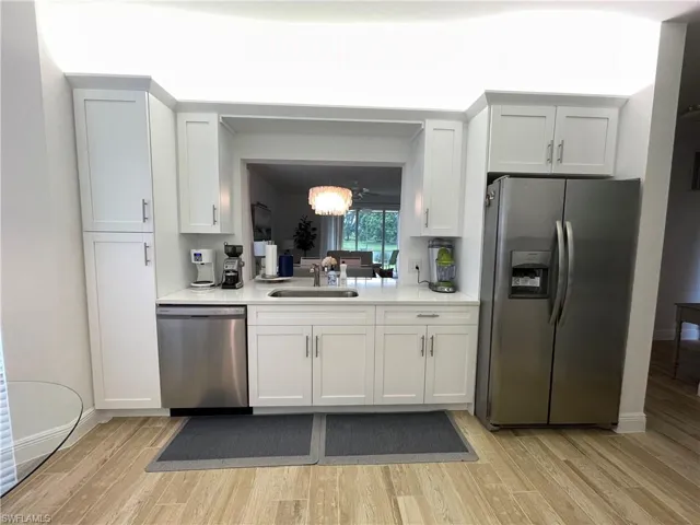 Kitchen featuring stainless steel appliances, white cabinets, light wood-type flooring, light stone counters, and a chandelier