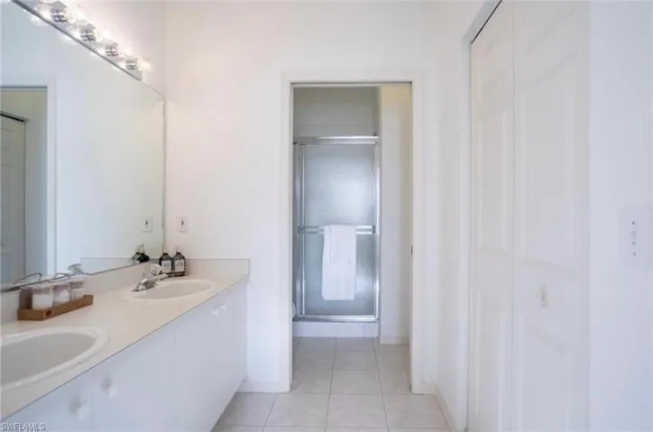 Primary Bathroom with double vanity, a walk in closet, a shower stall, and light tile patterned floors