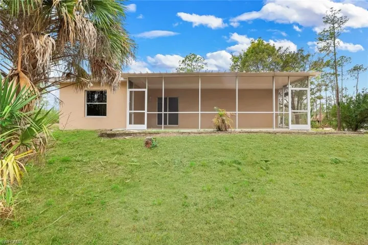 Back of house with a sunroom, a lawn, and stucco siding