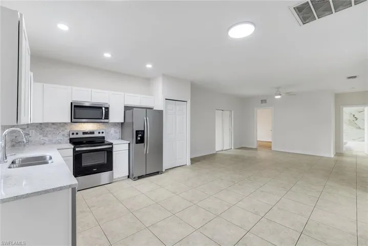 Kitchen featuring stainless steel appliances, tasteful backsplash, white cabinetry, light stone countertops, and open floor plan