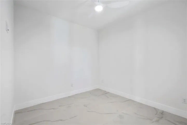 Spare room featuring marble finish floor, baseboards, and a ceiling fan