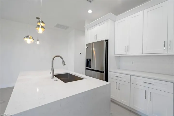 Kitchen featuring visible vents, pendant lighting, stainless steel refrigerator with ice dispenser, a sink, and white cabinets