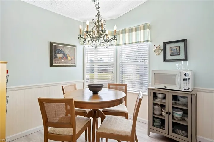 Dining space featuring a wainscoted wall, light wood-style flooring, a textured ceiling, crown molding, and a chandelier
