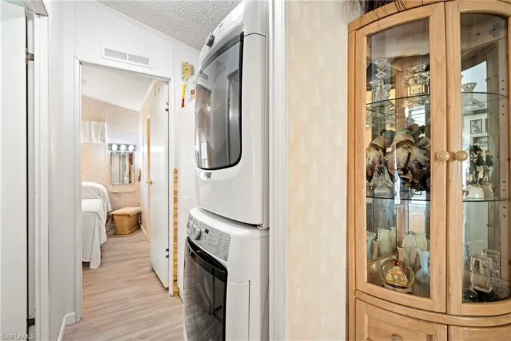 Laundry area featuring stacked washer / drying machine, a textured ceiling, and light wood finished floors