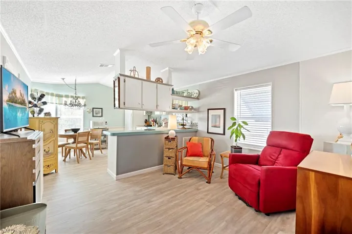 Living room featuring a textured ceiling, light wood finished floors, ornamental molding, a chandelier, and lofted ceiling