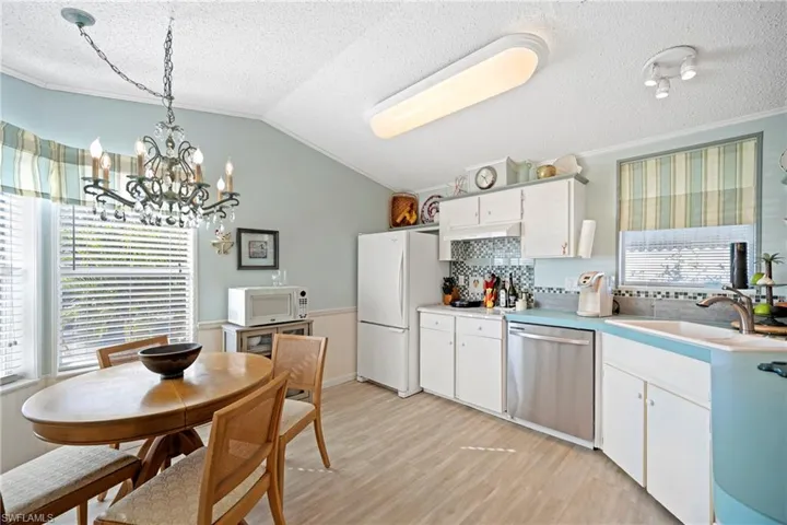 Kitchen featuring white cabinets, light countertops, backsplash, white appliances, and pendant lighting