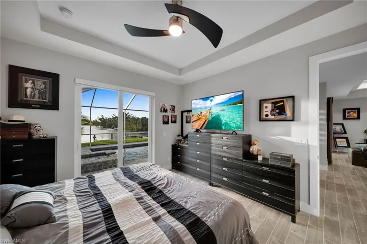 Bedroom featuring access to exterior, light hardwood / wood-style floors, a raised ceiling, and ceiling fan