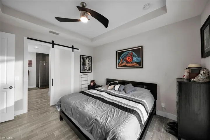 Bedroom with a tray ceiling, a barn door, ceiling fan, and light hardwood / wood-style flooring