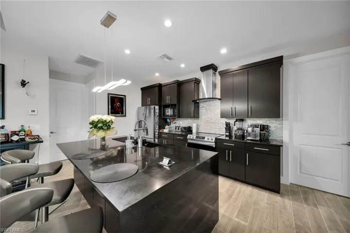 Kitchen with a kitchen island with sink, light hardwood / wood-style flooring, decorative light fixtures, and wall chimney range hood
