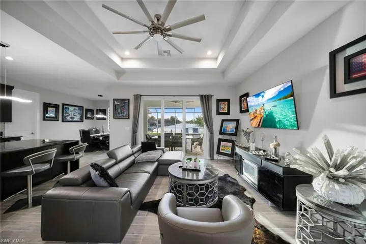 Living room featuring a tray ceiling, ceiling fan, light hardwood / wood-style flooring, and indoor bar